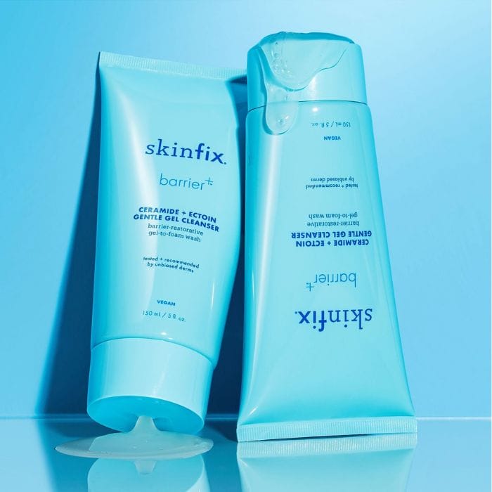 Skinfix-Barrier-Gentle-Gel-Cleanser5 Na obrazku znajdują się dwa opakowania produktu Skinfix Barrier+ Ceramide + Ectoin Gentle Gel Cleanser. Produkt jest przedstawiony w dwóch wersjach opakowania: tubce i butelce z pompką. Tubka po lewej stronie ma jasno niebieski kolor i jest otwarta, z niewielką ilością produktu wyciśniętą na powierzchnię. Na tubce widnieje napis "skinfix barrier+ CERAMIDE + ECTOIN GENTLE GEL CLEANSER barrier-restorative gel-to-foam wash tested + recommended by unbiased derms VEGAN 150 mL / 5 fl. oz." Butelka z pompką po prawej stronie ma również jasno niebieski kolor i leży na boku. Na butelce znajduje się ten sam tekst co na tubce, odwrócony do góry nogami. Oba opakowania są przedstawione na niebieskim tle, a całość kompozycji podkreśla świeżość i czystość produktu.