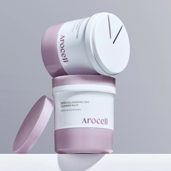 Arocell Super Collagen Melting Cleansing Balm Zdjęcie przedstawia dwa opakowania balsamu Arocell Super Collagen Melting Cleansing Balm. Opakowania mają elegancki design w odcieniach fioletu i bieli. Jedno opakowanie stoi pionowo z otwartą pokrywką, a drugie jest pochylone na jego powierzchni, ukazując unikalny mechanizm dozowania produktu na górnej części wieczka. Minimalistyczny styl podkreśla luksusowy charakter produktu, a opis na opakowaniu wskazuje na jego delikatne i odżywcze właściwości.