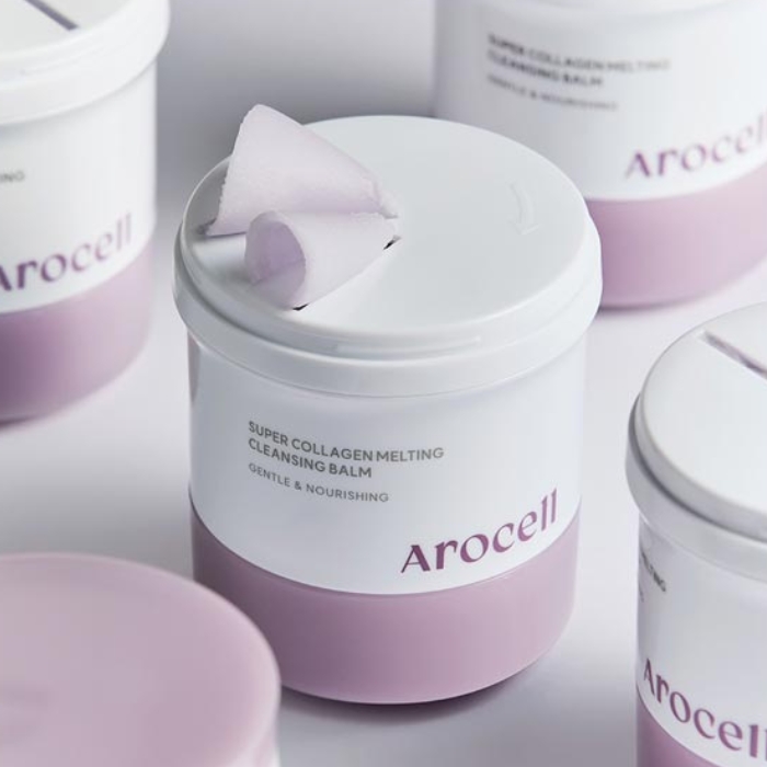 Arocell Super Collagen Melting Cleansing Balm Zdjęcie przedstawia kilka opakowań balsamu Arocell Super Collagen Melting Cleansing Balm. Na pierwszym planie widoczne jest jedno opakowanie z unikalnym mechanizmem dozowania, na którym znajduje się wyciśnięty fragment balsamu w formie zwiniętej spirali. Produkt ma eleganckie, minimalistyczne opakowanie w odcieniach fioletu i bieli. W tle widać kolejne opakowania, co podkreśla profesjonalny charakter prezentacji produktu.