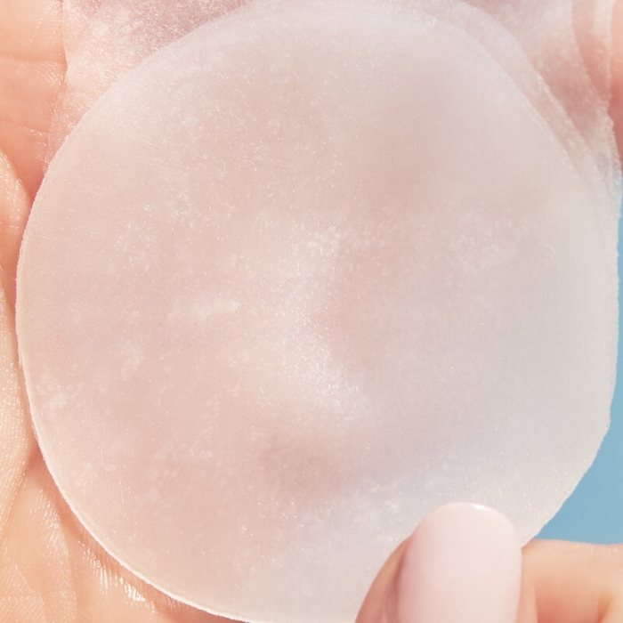 Peach Lily Cryo Reset Calming Mask Pads (2) Zbliżenie na pojedynczy płatek maski trzymany w dłoni. Płatek jest delikatny, lekko nasączony, co podkreśla jego nawilżające i chłodzące właściwości.