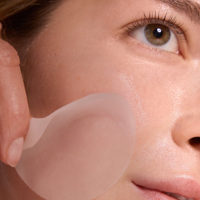 Peach Lily Cryo Reset Calming Mask Pads (4) Zbliżenie na twarz osoby aplikującej płatek maski na policzek. Płatek jest cienki, przezroczysty i idealnie dopasowuje się do kształtu twarzy, zapewniając równomierne działanie składników.