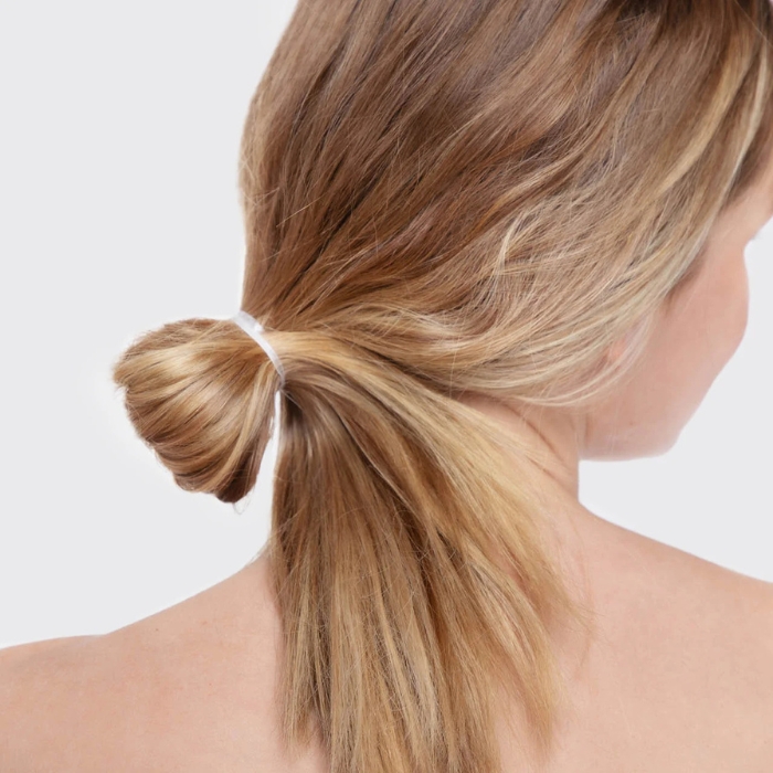 Kitsch No Snag Elastic (4) Modelka z blond włosami, z niskim kucykiem związanym jedną przezroczystą gumką, podkreślającą prostotę i elegancję fryzury.