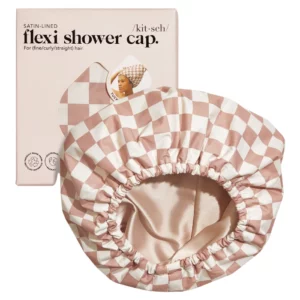 Na zdjęciu znajduje się różowo-biała czepka w kratkę z satynowym wnętrzem, wraz z opakowaniem produktu "Flexi Shower Cap".