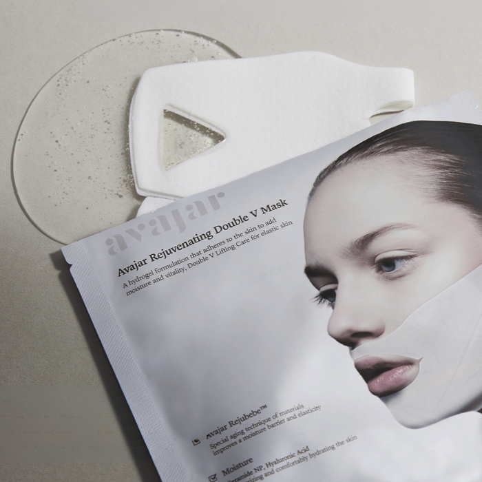 Avajar Rejuvenating Double V Mask 1 Otwarte opakowanie maski modelującej Rejuvenating Double V Mask. marki Avajar, z wyciągniętą maseczką i plamą wody, która sugeruje nawilżające działanie produktu.