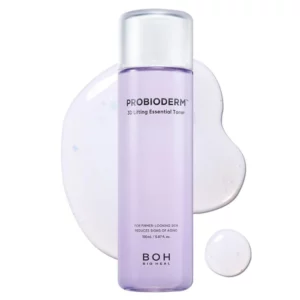 Fioletowa butelka toniku BOH Probioderm 3D Lifting Essential Toner otoczona kropelkami lekkiego, półprzezroczystego płynu z niebieskimi drobinkami.