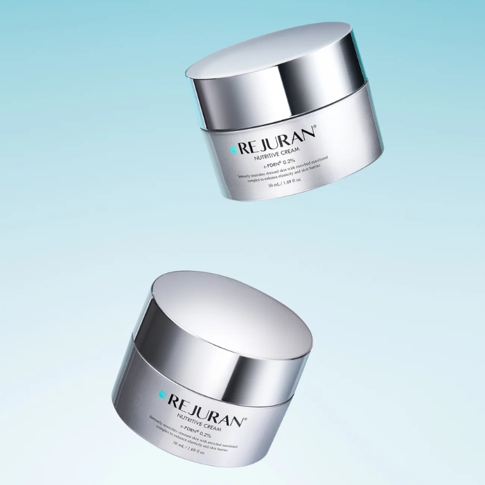 rejuran healer cream (3) Dwa eleganckie słoiczki REJURAN Nutritive Cream w metalicznym srebrnym wykończeniu, unoszące się na błękitnym tle.