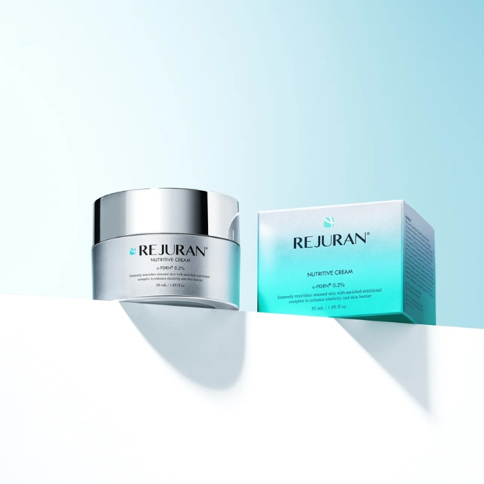 rejuran healer cream (4) Słoiczek REJURAN Nutritive Cream obok turkusowo-srebrnego opakowania, ustawiony na białej powierzchni z subtelnym cieniem.