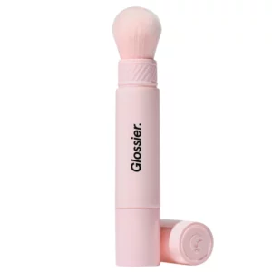 Pojedynczy pędzel Glossier Cloud Paint Cheek Brush w jasnoróżowej oprawie z zakrętką obok.