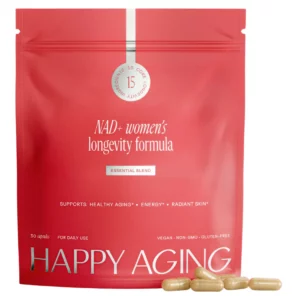 Czerwona saszetka NAD+ women’s longevity formula Essential Blend z widocznym logo HAPPY AGING oraz napisem „15 core longevity ingredients”, ustawiona na jasnym tle wraz z kilkoma kapsułkami.