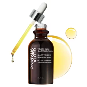 Na obrazie widoczna jest ciemna szklana butelka serum z napisem IOPE, obok której znajduje się pipeta z jasnym płynem oraz kropla serum na jasnym tle.