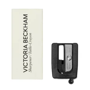 Temperówka do kredek Victoria Beckham Pencil Sharpener z ostrzem ze stali nierdzewnej oraz beżowym opakowaniem z logo marki, prezentowana na białym tle.