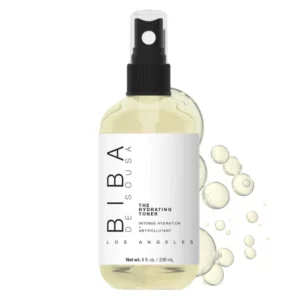 Butelka Biba Los Angeles The Hydrating Toner 236 ml z atomizerem, w przezroczystym opakowaniu z jasnożółtym tonikiem. Minimalistyczna, biała etykieta z czarnym napisem „BIBA The Hydrating Toner - Intense Hydration + Antipollutant”. Obok produktu widoczne krople płynu na jasnym tle.