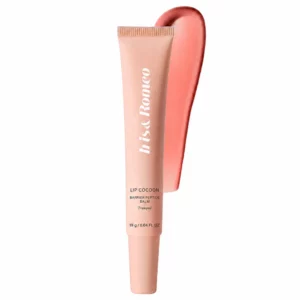 Różowa tubka balsamu do ust Iris & Romeo Lip Cocoon Barrier Peptide Balm w odcieniu Freedom, ustawiona pionowo na białym tle z błyszczącą różową smugą produktu za opakowaniem.