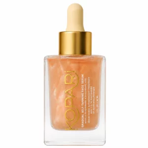 Szklana buteleczka z pipetą Kopari Gradual Self-Tanning Face Serum z 2% niacynamidem i kwasem hialuronowym, wypełniona połyskującym brzoskwiniowym serum, pokazana na białym tle.