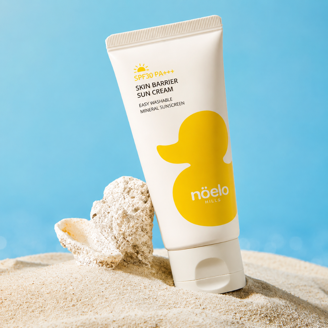 Noelo Hills Skin Barrier Sun Cream SPF 30 Noelo Hills Skin Barrier Sun Cream SPF30 PA+++ na piasku obok muszli. Mineralny krem przeciwsłoneczny dla niemowląt i dzieci.