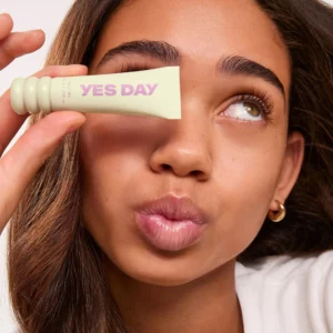 Kobieta z błyszczącymi ustami trzyma przy oku żółtą maskę do ust YES DAY Lip Sweetie Yuzu Sorbet 10 g.