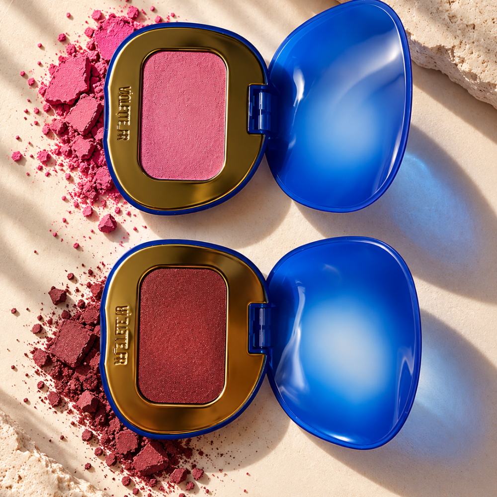 Violette FR Plume Blush Feather Matte Cheek Melt (2) Violette_FR Plume Blush Feather Matte Cheek Melt - dwa róże do policzków w różowym i głębszym czerwono-różowym odcieniu, pokazane w otwartych niebiesko-złotych opakowaniach z rozsypanym pigmentem.