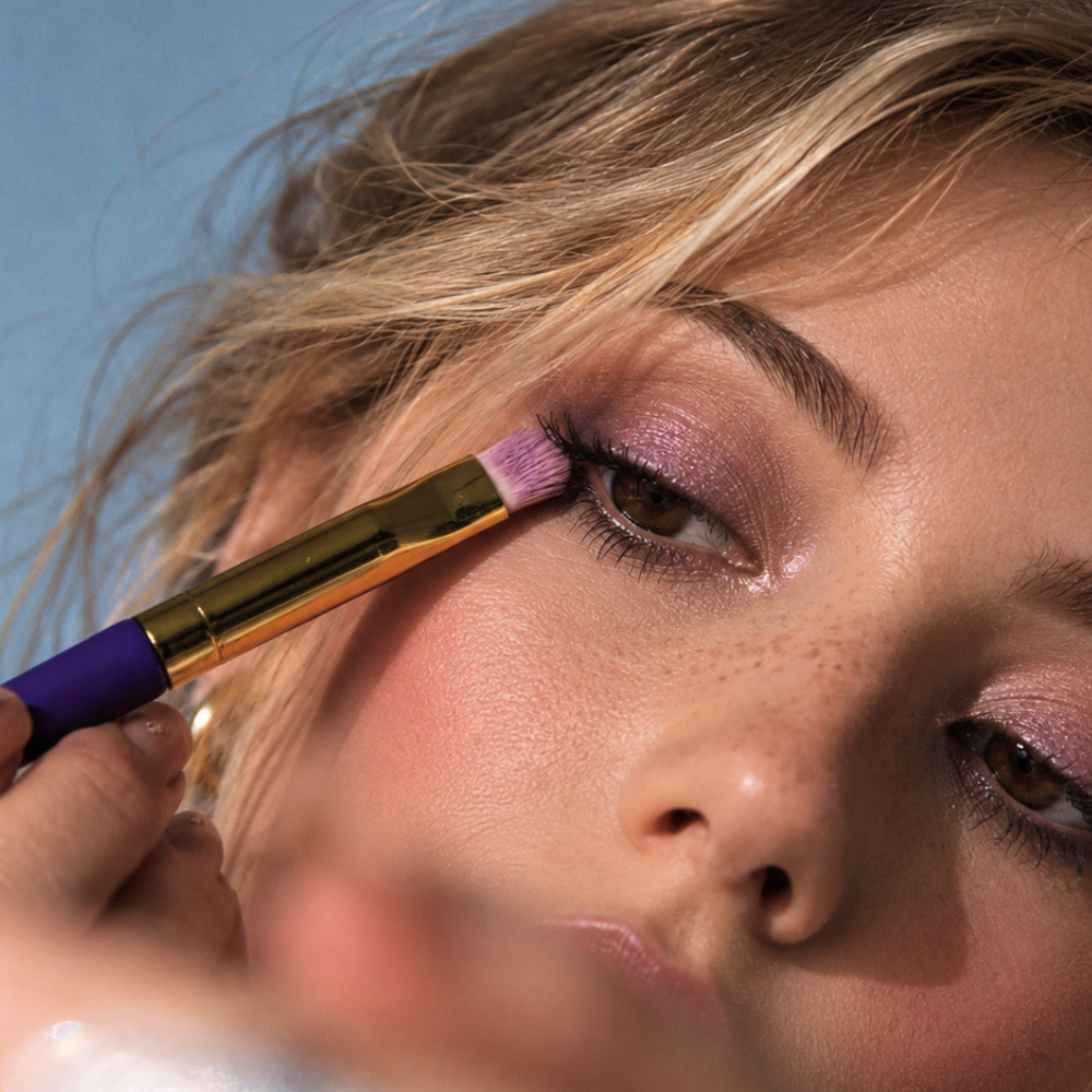 Violette FR Plume Eyeshadow (2) Violette_FR Plume Eyeshadow - zbliżenie na aplikację połyskującego różowo-fioletowego cienia na powiekę za pomocą pędzla. Makijaż oka w świetlistym, kobiecym wydaniu.