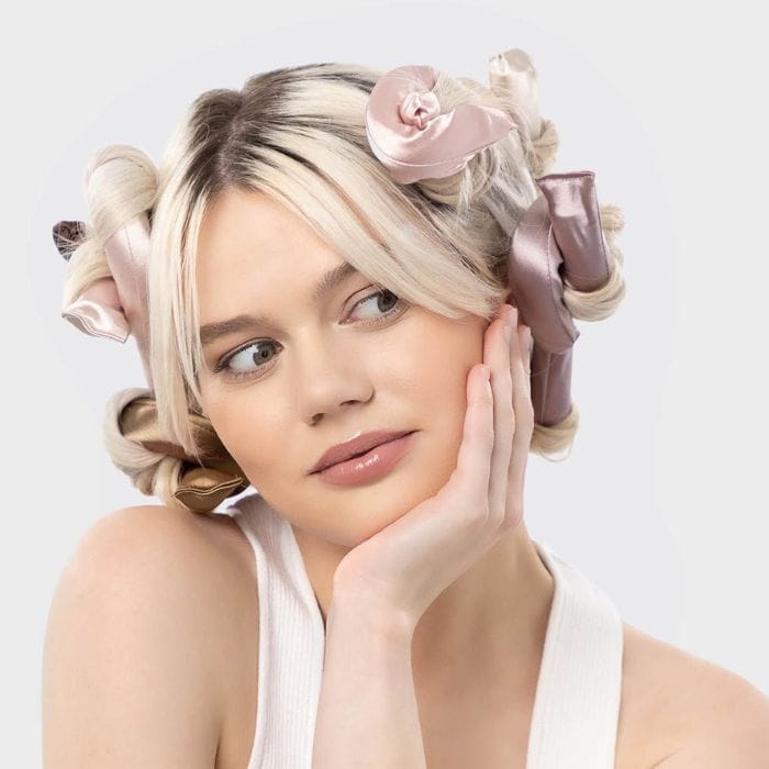 Kitsch Satin Flexi Rods Kobieta z jasnymi włosami stylizowanymi na Kitsch Satin Wrapped Flexi Rods w pastelowych odcieniach różu i beżu.
