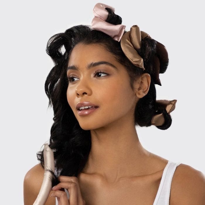 Kitsch Satin Flexi Rods Kobieta z ciemnymi włosami używająca Kitsch Satin Wrapped Flexi Rods w różowych i brązowych odcieniach do stylizacji loków.