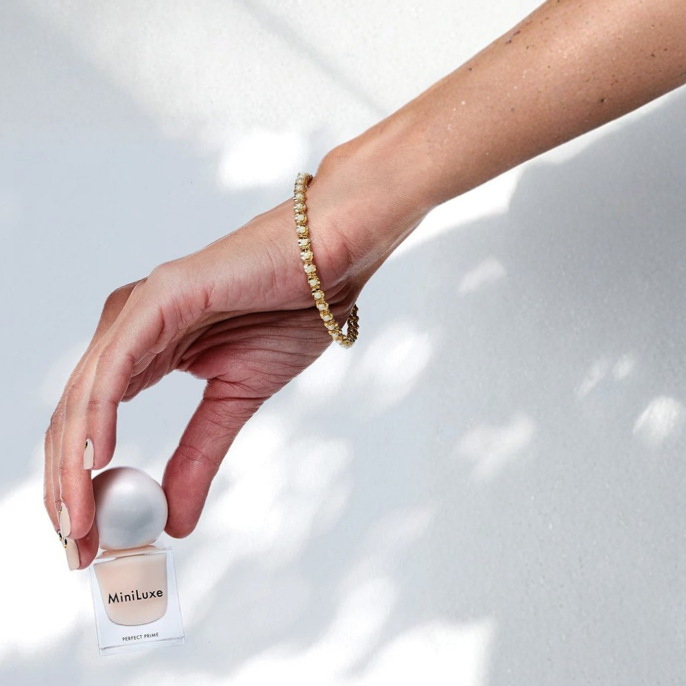 MiniLuxe Perfect Prime Base Coat MiniLuxe Perfect Prime Base Coat w eleganckiej szklanej buteleczce na rozświetlonym tle z miękkim cieniem.