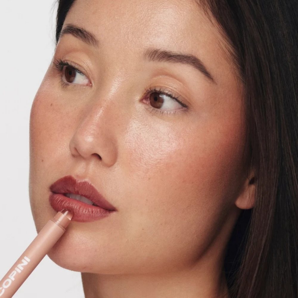 Copini Love Bite Soft Focus Lip Stain (5) Copini Love Bite Soft Focus Lip Stain - aplikacja - modelka podczas nakładania produktu na usta za pomocą precyzyjnego aplikatora w kredce.