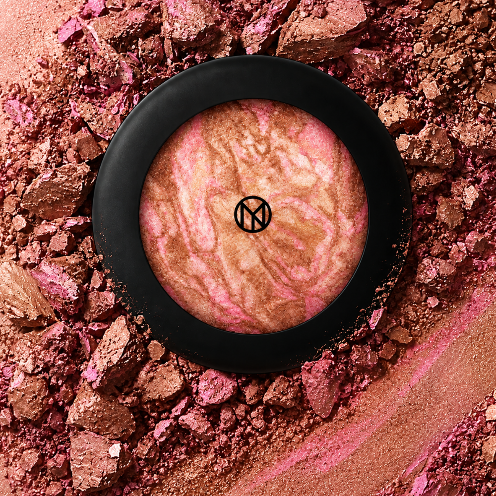 IL MAKIAGE Mineral Baked Bronzer - mineralny wypiek słońca (4) IL MAKIAGE Mineral Baked Bronzer w odcieniu Touch Me - marmurkowy bronzer w różowo-brązowo-złotych tonach, w czarnym okrągłym opakowaniu, otoczony rozkruszonym i rozsypanym pigmentem.
