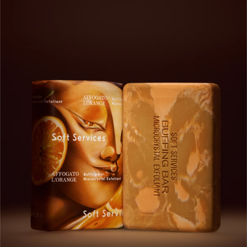 Soft Services Affogato L'Orange Buffing Bar Exfoliant (5) Soft Services Affogato L'Orange Buffing Bar - mikrokrystaliczna kostka peelingująca do ciała w karmelowo-brązowym kolorze, zaprezentowana obok opakowania Affogato L'Orange.