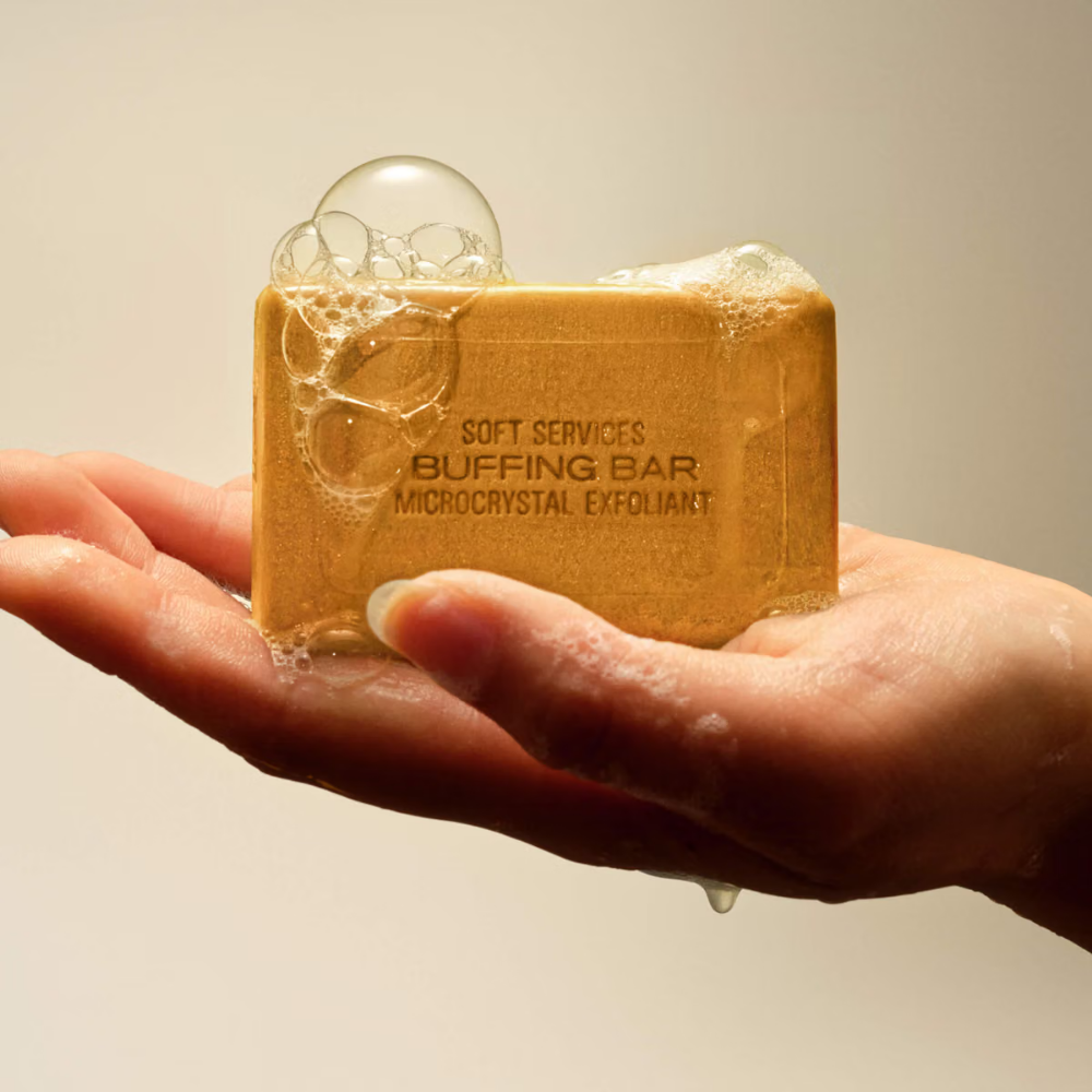 Soft Services X Vacation Buffing Bar Exfoliant - kostka peelingująca pachnąca jak najlepsze wakacje (4) Soft Services x Vacation Buffing Bar - złuszczanie skóry ciała - spieniona złocista kostka peelingująca Soft Services Buffing Bar trzymana w mokrej dłoni podczas stosowania pod prysznicem.
