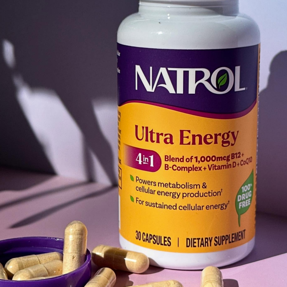 Natrol Ultra Energy 4-in-1, Natrol Ultra Energy 4 in 1 - suplement diety z witaminą B12, witaminą D, kompleksem witamin B i koenzymem Q10. Butelka z fioletowo-pomarańczową etykietą oraz beżowe kapsułki przedstawione na fioletowym tle.