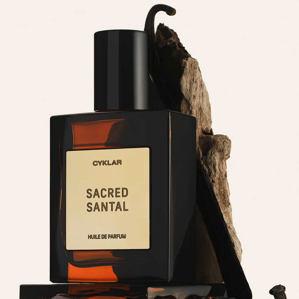 Cyklar The Bestsellers Perfume Oil Set (4) CYKLAR Sacred Santal Perfume Oil - luksusowy olejek perfumowany o ciepłej, drzewnej kompozycji zapachowej, w eleganckim bursztynowym flakonie na tle drewna sandałowego.