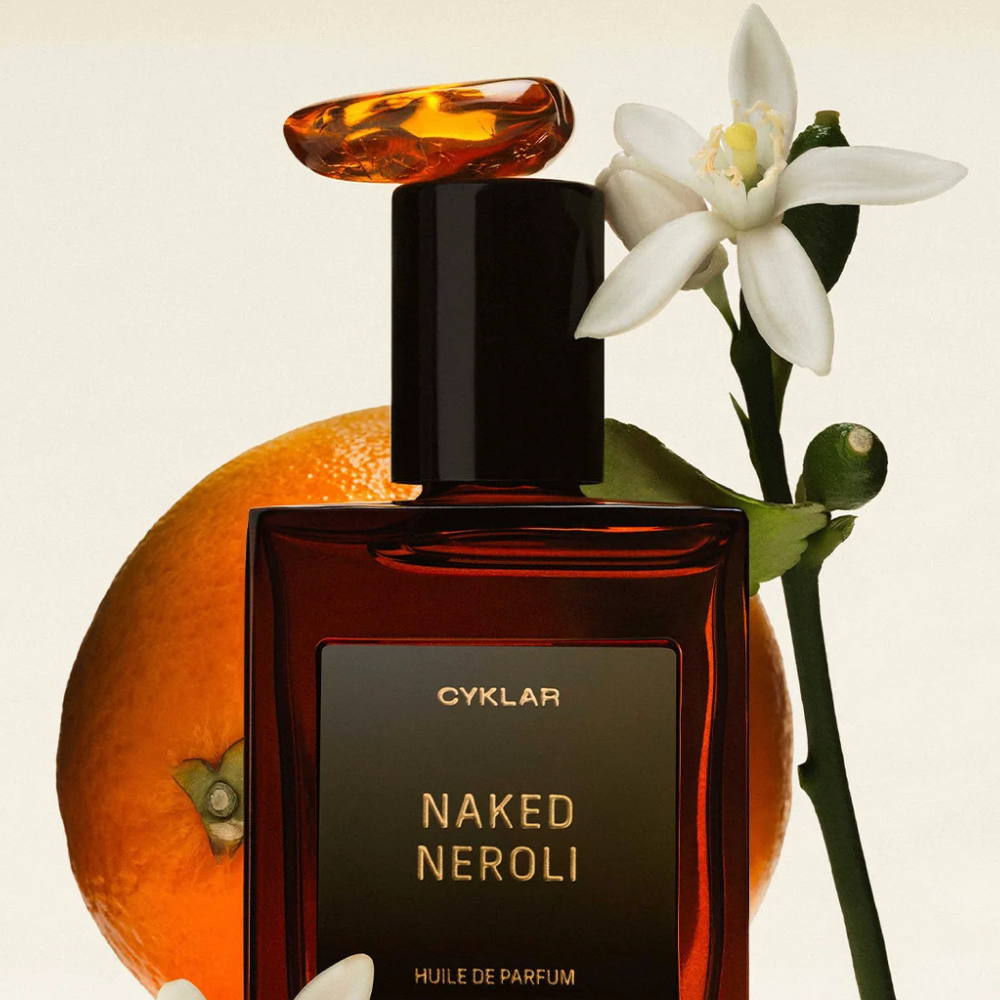 Cyklar The Bestsellers Perfume Oil Set (6) CYKLAR Naked Neroli Perfume Oil - olejek perfumowany o świeżym, cytrusowo-kwiatowym zapachu neroli, w bursztynowym flakonie na tle pomarańczy i białych kwiatów.