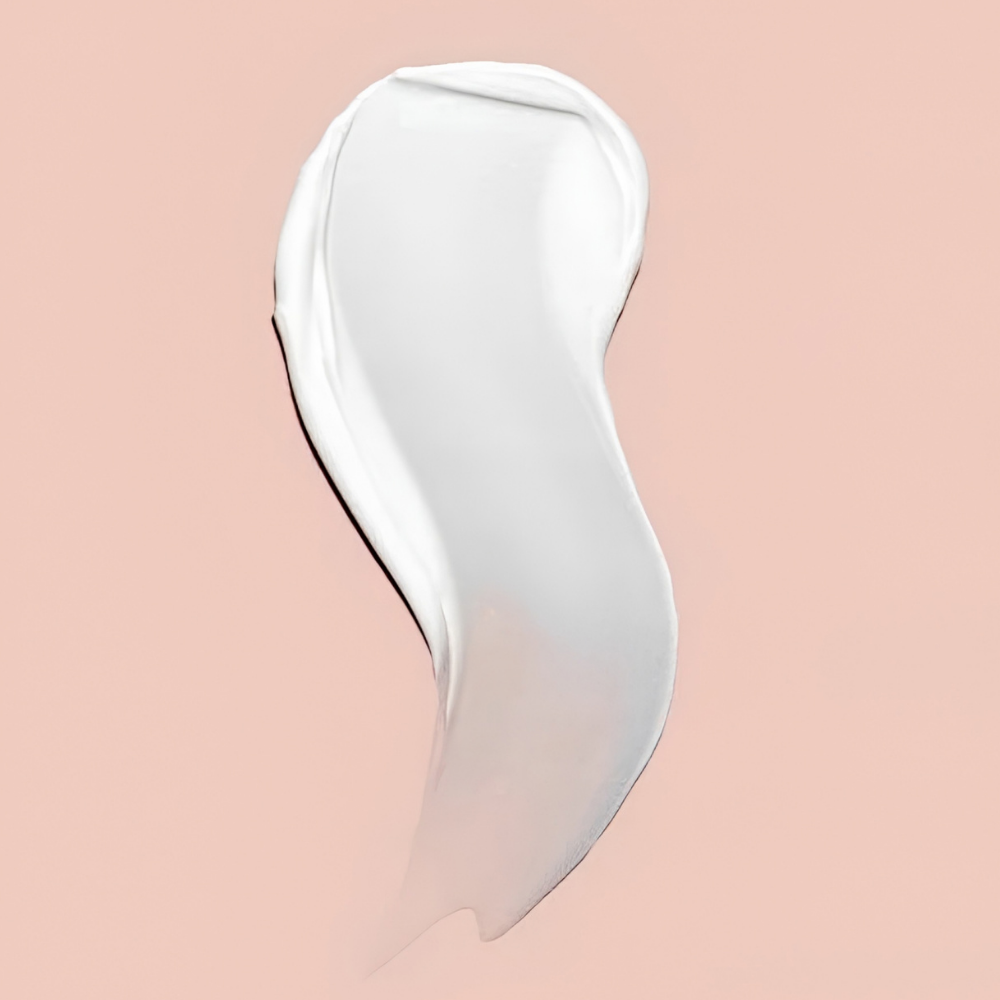 Glo Skin Beauty Hydra Bright AHA Hydrator (3) Glo Skin Beauty Hydra-Bright AHA Hydrator - zbliżenie na jedwabistą, kremową konsystencję na pasteloworóżowym tle. Biała, gładko rozprowadzona formuła nawilżającego kremu rozświetlającego z kwasem mlekowym AHA i witaminą C.