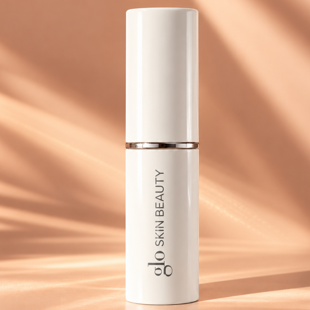 Glo Skin Beauty Skin Glow Stick Highlighter (2) Glo Skin Beauty Skin Glow Stick Highlighter - kremowy rozświetlacz w sztyfcie w eleganckim, zamkniętym biało-srebrnym opakowaniu z logo marki, na brzoskwiniowym tle z subtelnymi refleksami światła, luksusowy kosmetyk do rozświetlania twarzy.
