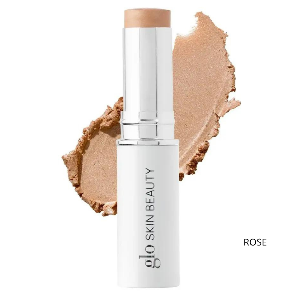 Glo Skin Beauty Skin Glow Stick Highlighter (7) Glo Skin Beauty Skin Glow Stick Highlighter Rose - kremowy rozświetlacz w sztyfcie w delikatnym różowo-złotym odcieniu, biało-srebrne opakowanie z logo marki i próbka połyskującej konsystencji na białym tle, efekt naturalnego rozświetlenia skóry.
