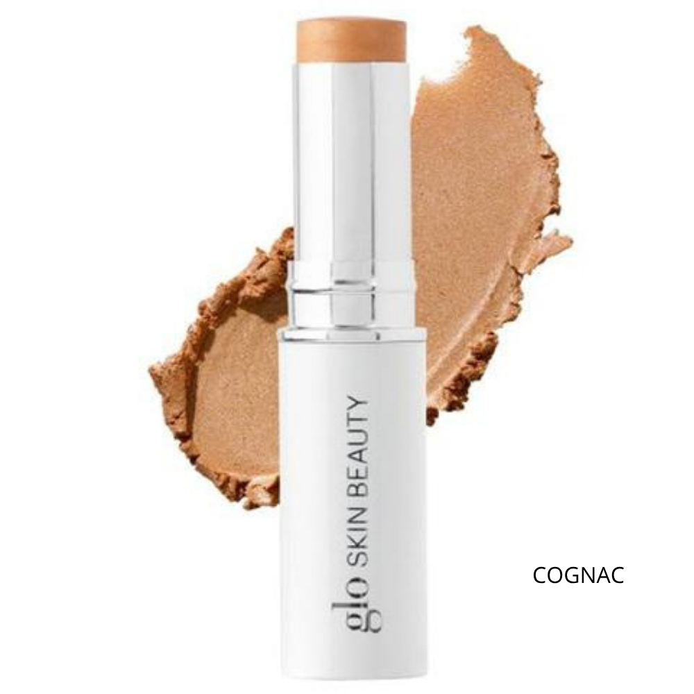 Glo Skin Beauty Skin Glow Stick Highlighter (8) Glo Skin Beauty Skin Glow Stick Highlighter Cognac - kremowy rozświetlacz w sztyfcie w ciepłym, brązowo-złotym odcieniu, biało-srebrne opakowanie z logo marki oraz próbka połyskującej konsystencji na białym tle, efekt złocistego rozświetlenia skóry.
