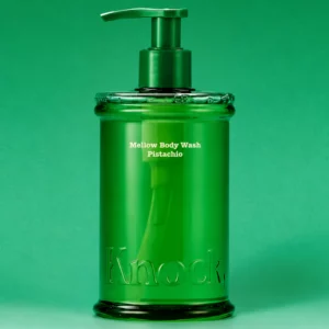 Knock Mellow Body Wash Pistachio 300 ml - pistacjowy żel pod prysznic w eleganckiej, transparentnej zielonej butelce z pompką i wytłoczonym logo Knock, przedstawiony na zielonym tle.