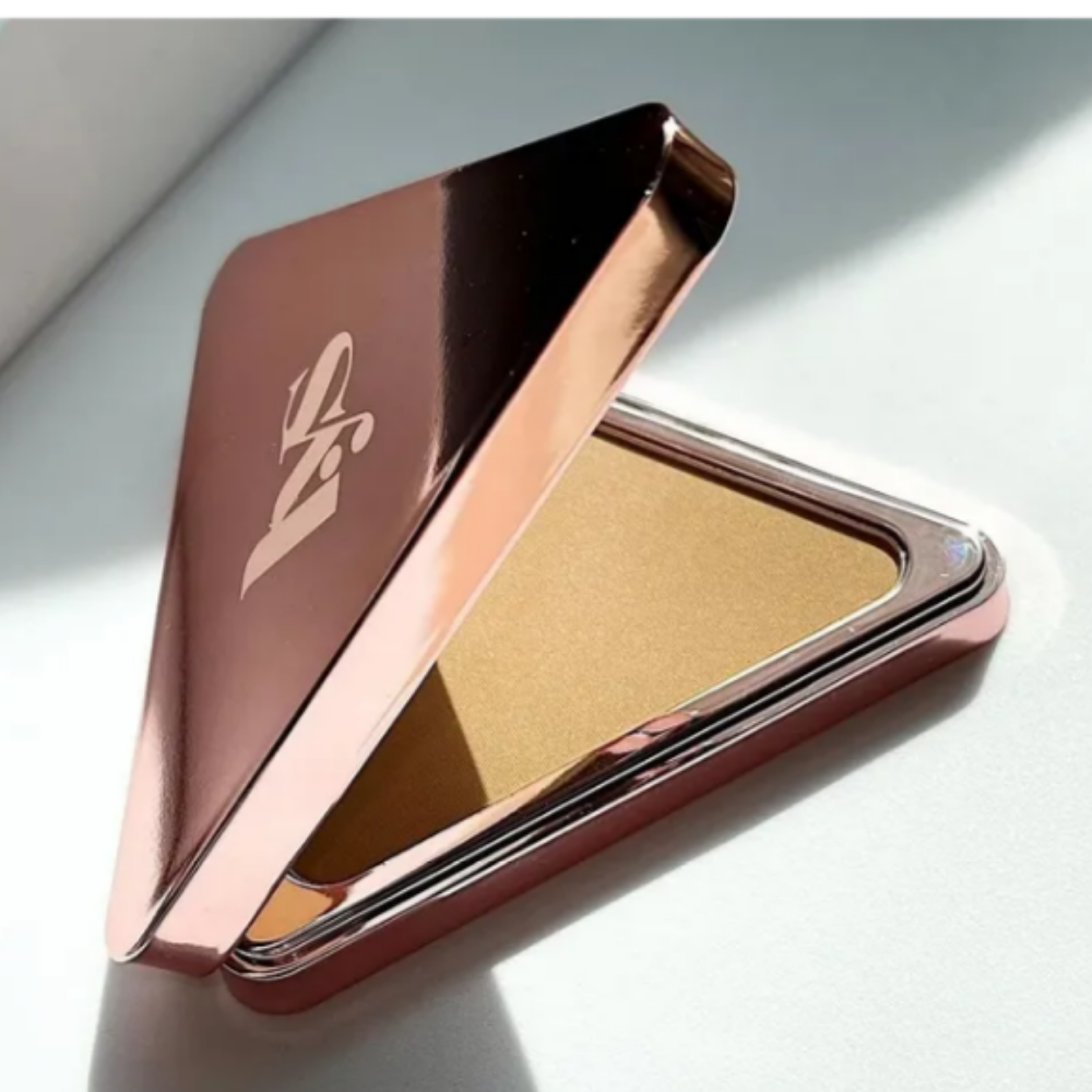 LYS Beauty Triple Fix Translucent Setting Powder LYS Beauty Triple Fix Translucent Pressed Setting Powder - transparentny puder prasowany utrwalający makijaż w luksusowym, trójkątnym opakowaniu w kolorze różowego złota. Otwarte opakowanie z widocznym pudrem w jasnobeżowym odcieniu, prezentowane w naturalnym świetle na jasnym tle.