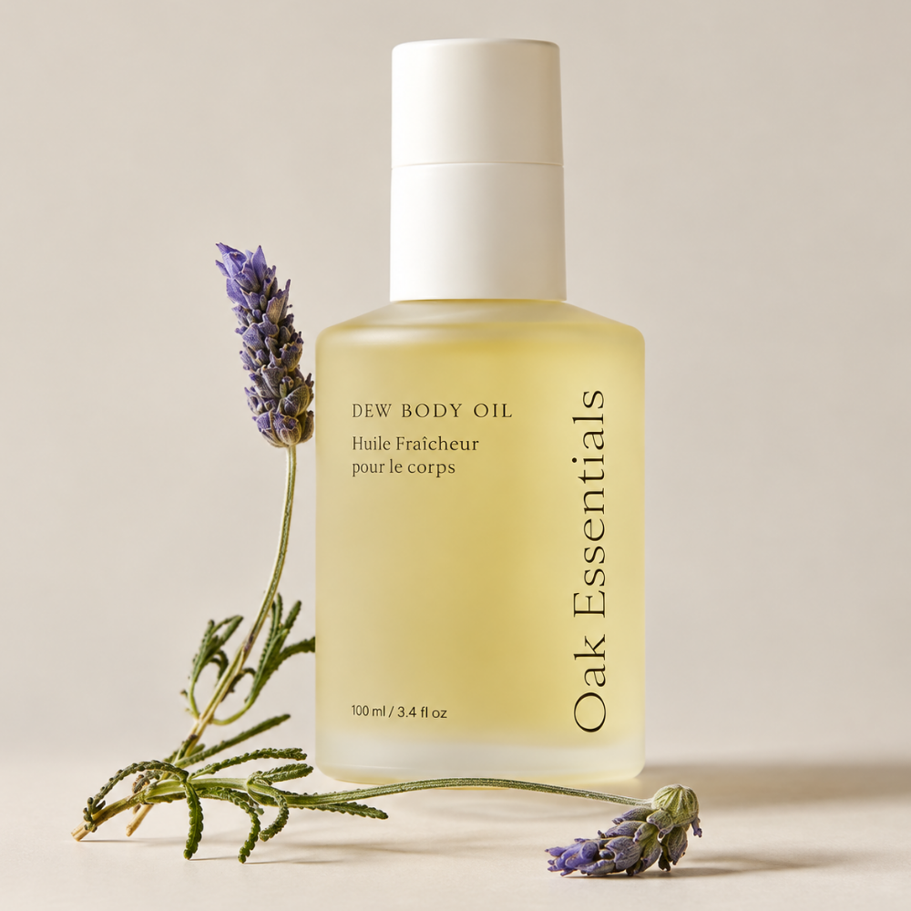 Oak Essentials Dew Body Oil (6) Oak Essentials Dew Body Oil 100 ml - olejek do ciała w eleganckiej szklanej butelce, przedstawiony z gałązkami lawendy na beżowym tle.