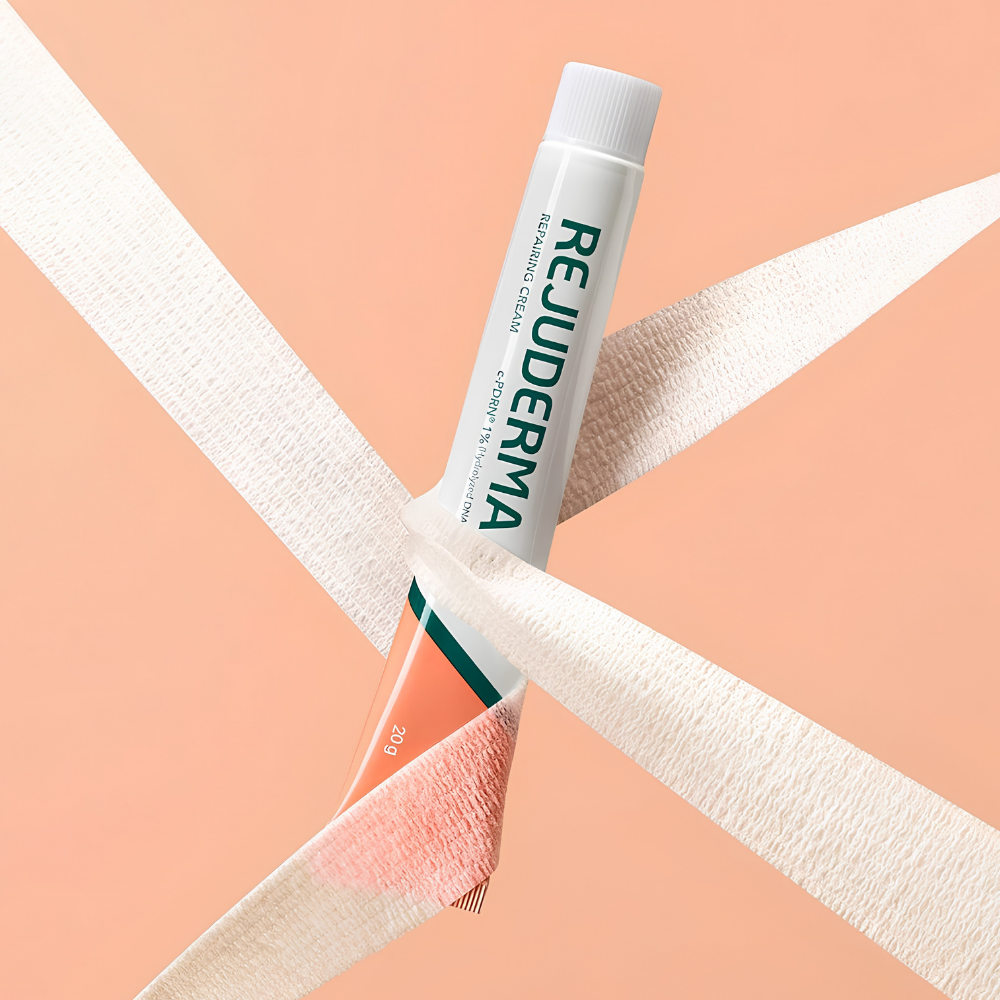 Rejuderma Ex Repairing Cream c PDRN 1% (2) REJUDERMA EX Repairing Cream c-PDRN 1% - koreański krem kojąco-odbudowujący do twarzy, biało-koralowa tubka 20 g z zielonym logo, otoczona białymi opatrunkowymi taśmami na brzoskwiniowym tle, symbolizującymi ukojenie i pielęgnację osłabionej skóry.
