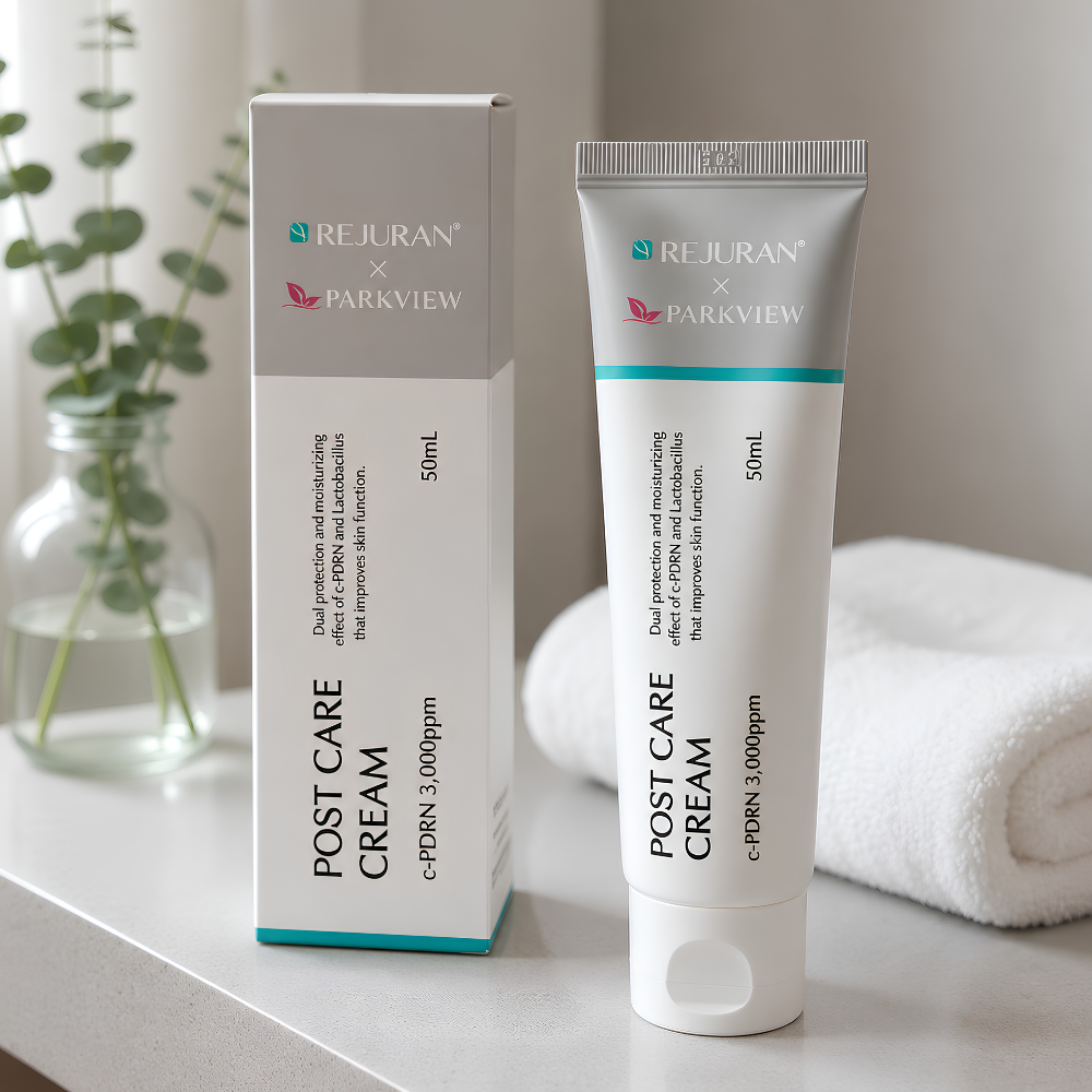 Rejuran X Parkview Post Care Cream (2) REJURAN x PARKVIEW Post Care Cream c-PDRN 3000 ppm - Koreański krem regenerujący i kojący do twarzy, 50 ml, w srebrno-białej tubce obok opakowania, na tle białego ręcznika i zielonego eukaliptusa.