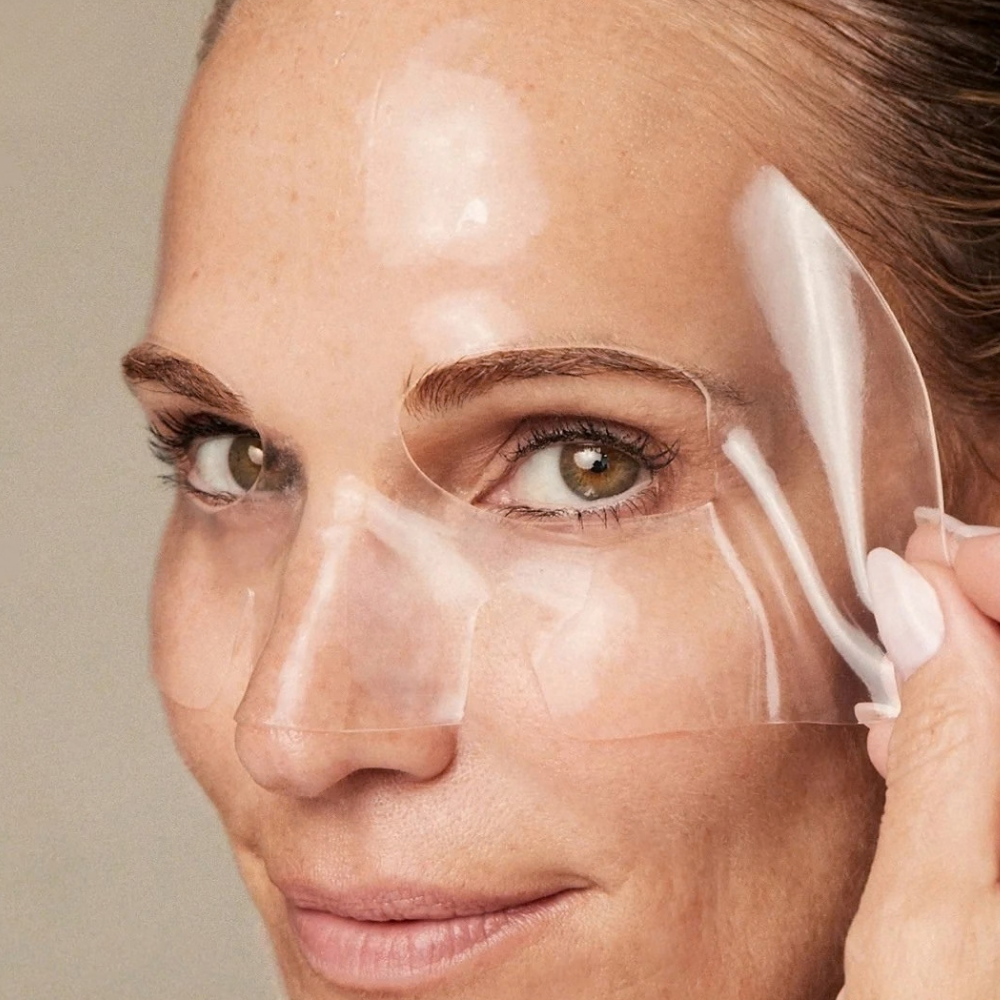 YSE Xtreme Glass Vegan PDRN Hydrogel Sheet Mask (3) YISE Beauty Xtreme Glass Vegan PDRN Hydrogel Sheet Mask - zbliżenie modelki zdejmującej transparentną maskę hydrożelową dopasowaną do konturów twarzy.