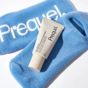 Prequel Foot Rescue Advanced Restorative Treatment - beżowa tubka regenerującego kremu do stóp ułożona na niebieskich, miękkich skarpetach z logo Prequel. Jasna fotografia produktowa podkreślająca pielęgnację suchej, szorstkiej i zrogowaciałej skóry stóp.