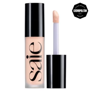 Korektor rozświetlający Saie Slip Tint Concealer w eleganckim opakowaniu z czarną zakrętką. Aplikator z gąbeczką jest nasączony produktem w jasnym odcieniu. Kosmetyk zdobył nagrodę Cosmopolitan Clean Beauty Awards.