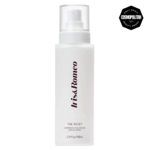 Na obrazku znajduje się biała butelka z serum w sprayu marki Iris&Romeo o nazwie "The Reset." Butelka ma prosty, elegancki design z napisem Iris&Romeo w pionie oraz nazwą produktu "The Reset Luminous Hyaluronic Serum Spray" u dołu. Obok butelki znajduje się czarny odznaka z napisem "Holy Grail Beauty Award" oraz logo magazynu Cosmopolitan.