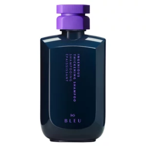 Na zdjęciu znajduje się butelka szamponu R+Co Bleu "Ingenious Thickening Shampoo". Produkt ma charakterystyczne, ciemne opakowanie z fioletową zakrętką, co wyróżnia go spośród innych kosmetyków. Na etykiecie widoczna jest nazwa produktu oraz logo marki.