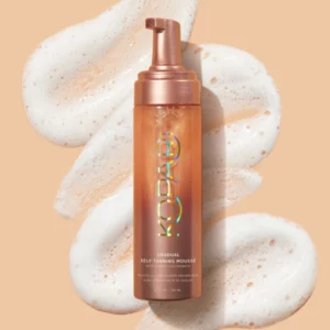 Zdjęcie przedstawia Kopari Gradual Self Tanning Mousse - samoopalającego musu o białym odcieniu. Opakowanie produktu ma brązowy i ciepły odcień.