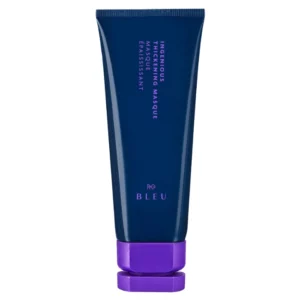 Na zdjęciu znajduje się maska do włosów w granatowej tubie z fioletową zakrętką. Na opakowaniu widoczny jest napis „Ingenious Thickening Masque” oraz marka „R+Co BLEU” w eleganckim, pionowym układzie. Tuba ma minimalistyczny i nowoczesny design.