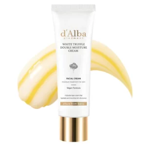 Na zdjęciu widzimy opakowanie kremu do twarzy d'Alba White Truffle Double Moisture Cream. Produkt znajduje się w białej tubce z eleganckimi złotymi i czarnymi elementami oraz logo marki. W tle widoczna jest kremowa konsystencja w dwóch odcieniach – jasnożółtym i białym, symbolizująca połączenie dwóch warstw formuły. Krem reklamowany jest jako wegański, zapewniający intensywne nawilżenie i odżywienie skóry.