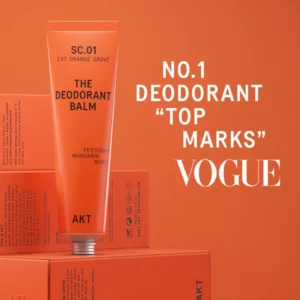 Pomarańczowa tuba dezodorantu AKT z napisem „No.1 Deodorant – Top Marks Vogue” na tle kartoników w tym samym kolorze.